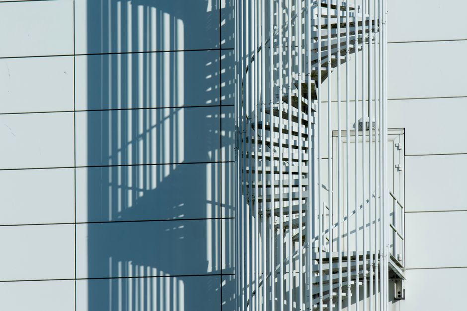 White spiral staircase casting shadows on building wall, showcasing modern urban architecture.