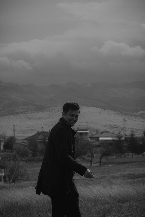 Free A black and white portrait of a smiling man standing in a rural countryside setting. Stock Photo