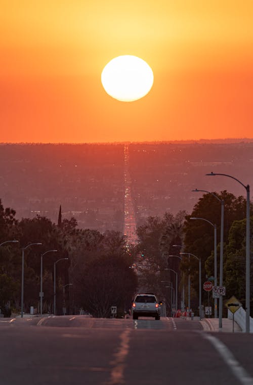 A sunset over a road with a car driving down it