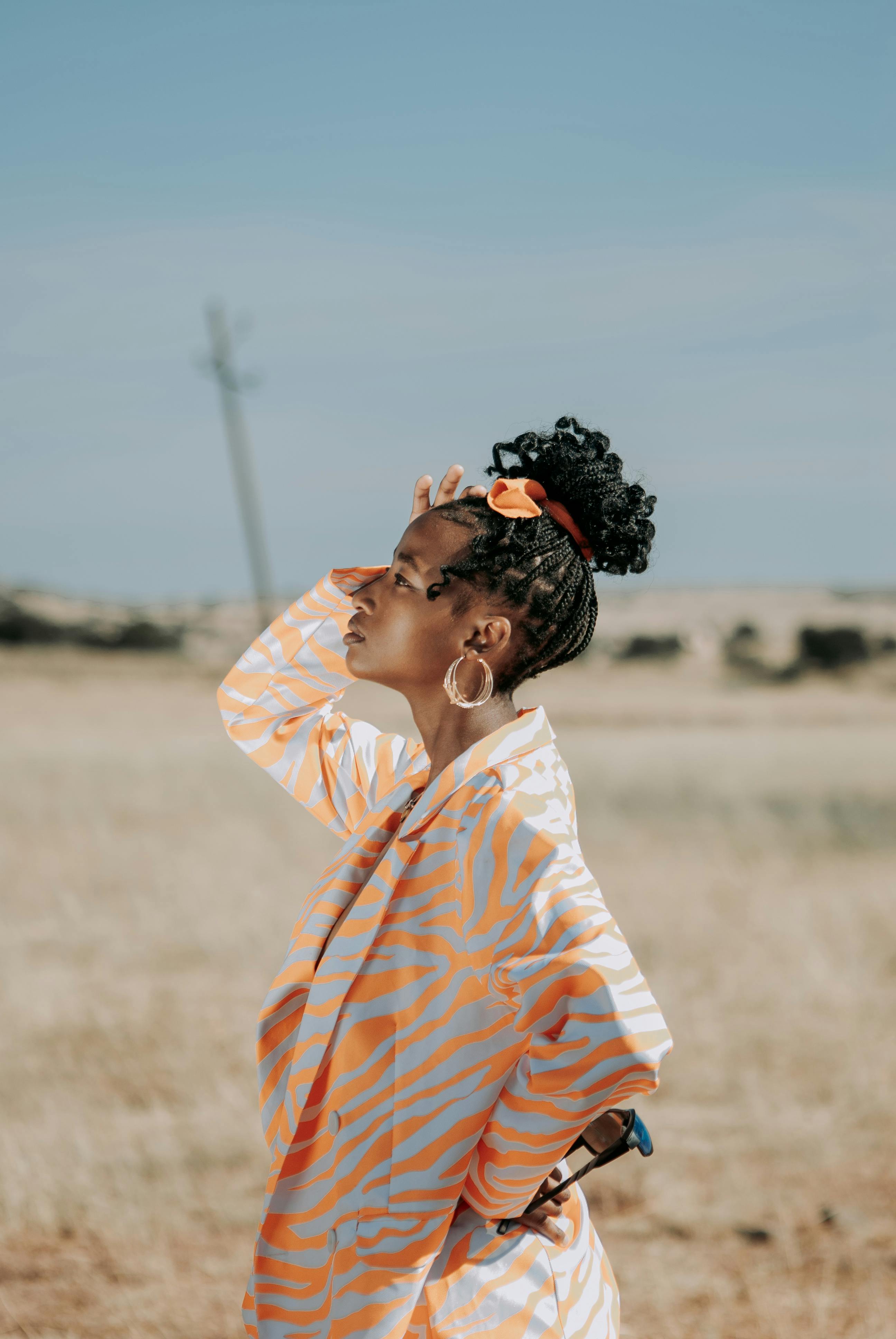 A fashionable young woman poses stylishly in a sunny meadow.