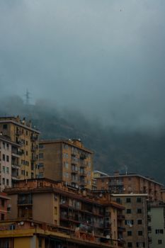 Foggy skyline of Genoa showcasing residential buildings against a mountainous backdrop.