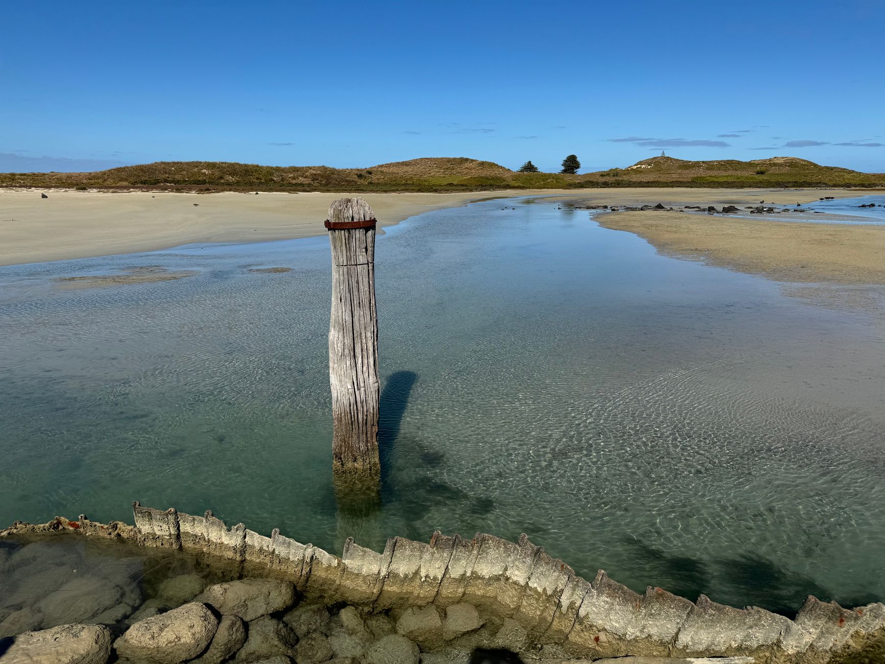 A tranquil coastal landscape with a wooden post and clear waters at Port Fairy, Victoria, Australia.