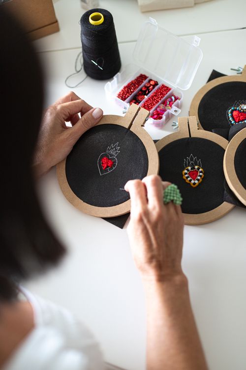 Woman using a punch needle to create colorful heart-shaped embroidery on stretched fabric