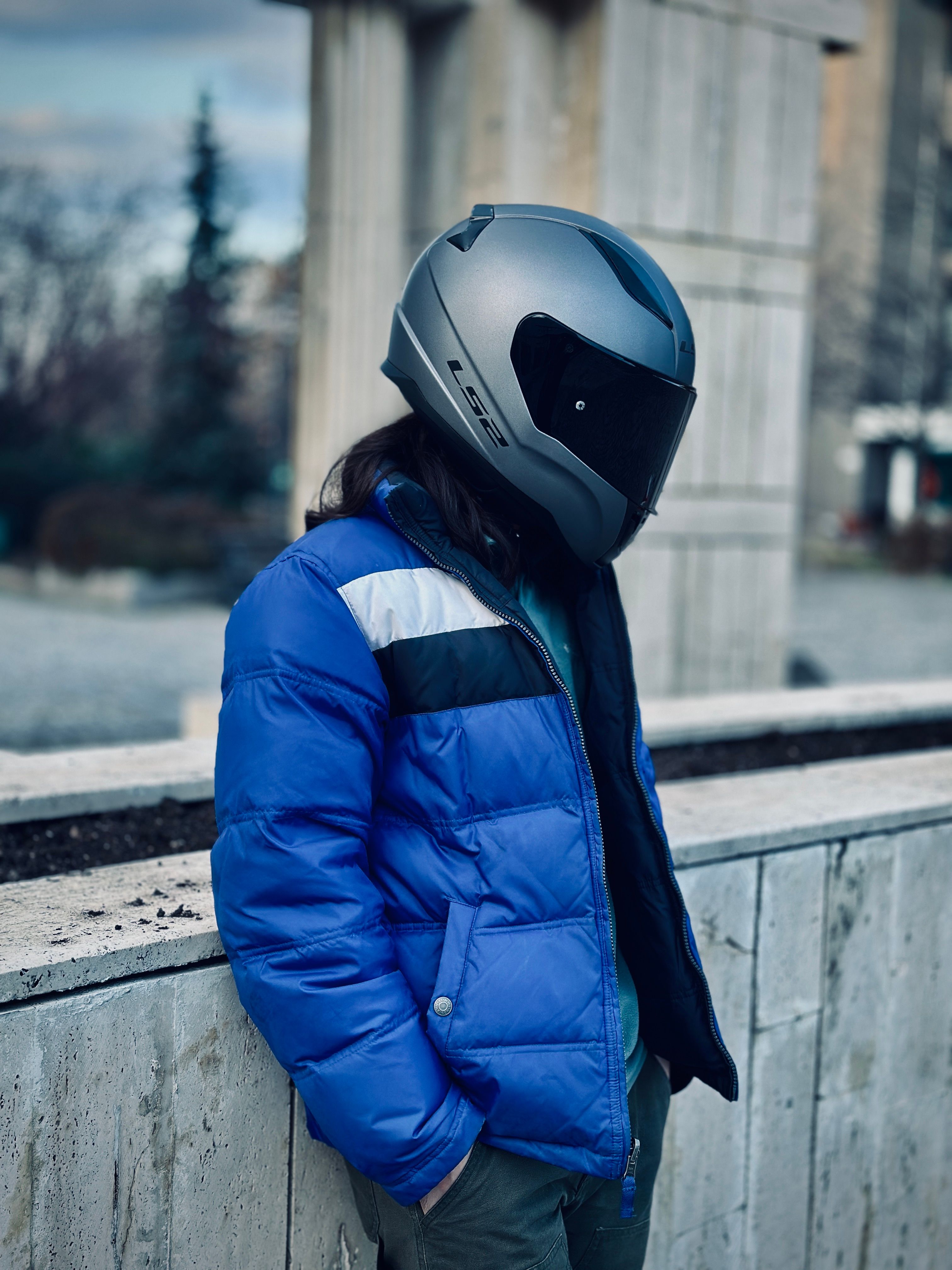 Person in a Helmet and a Jacket Standing by a Short Wall in a City ...