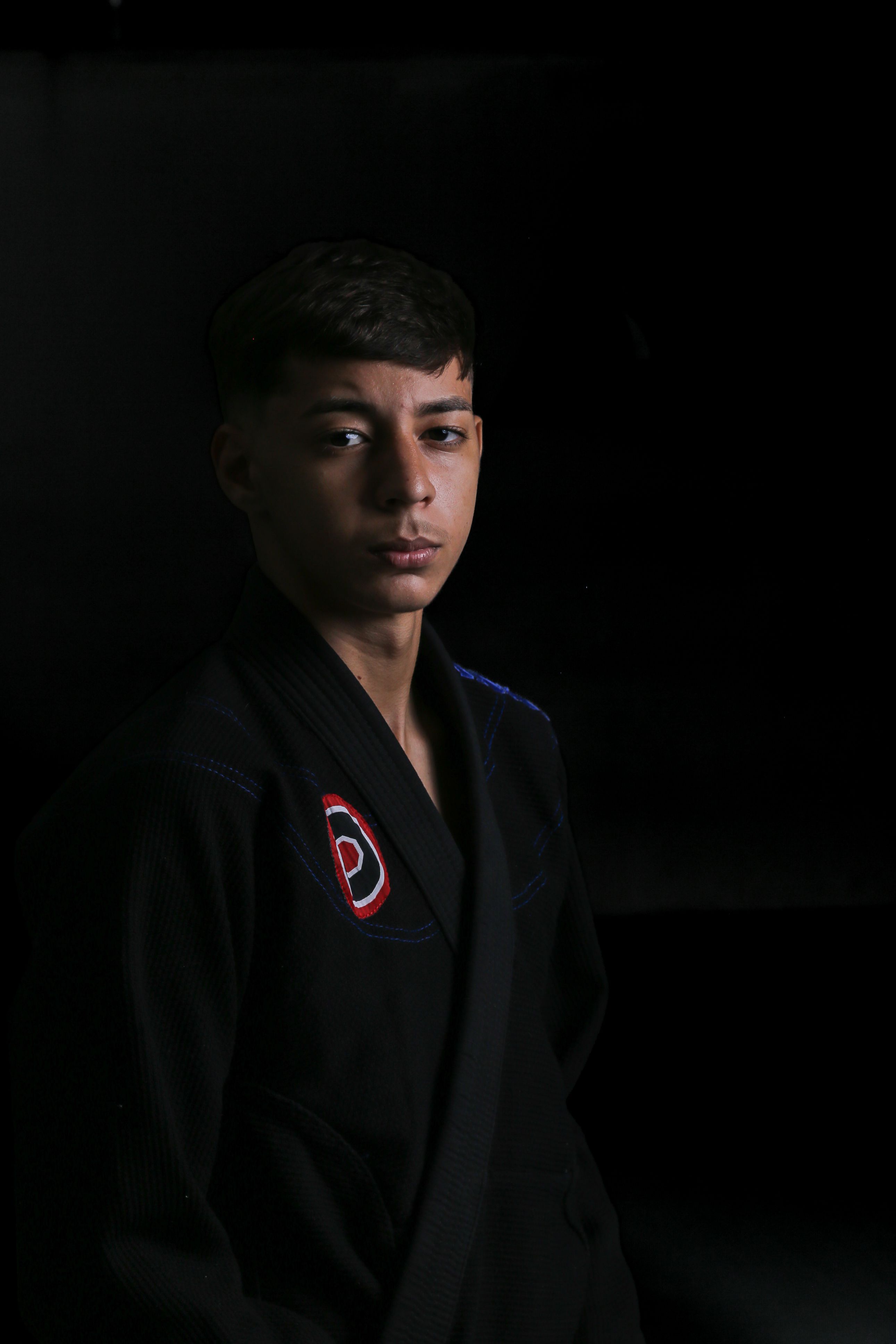 Young martial artist in a black gi posing confidently against a dark background.