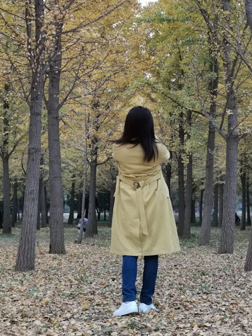 Woman Standing Back in a Yellow Trench Coat Against the Autumn Park Background