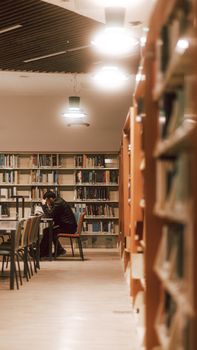 A man sitting at a table in a quiet, dimly lit library surrounded by bookshelves.