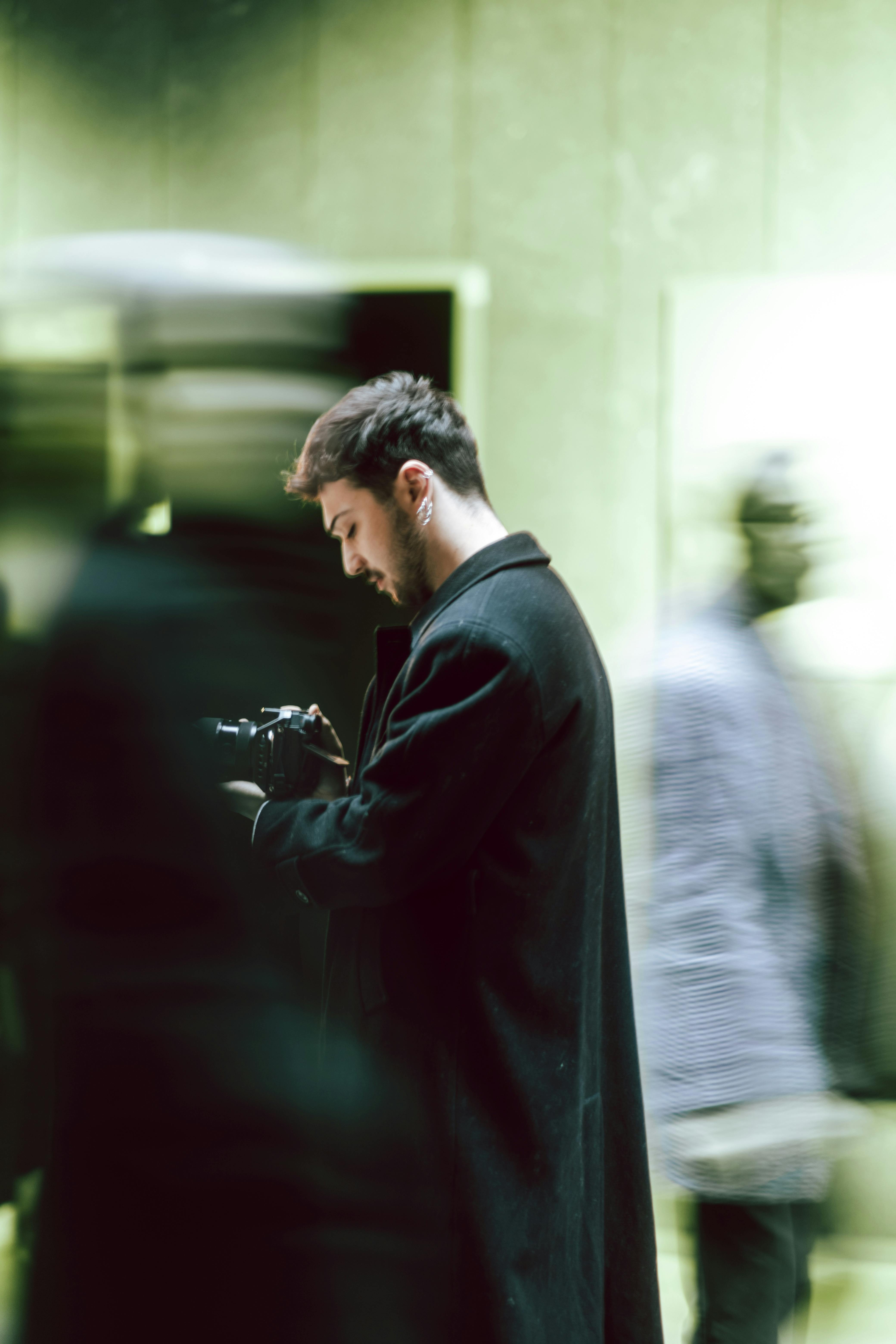A young man focuses on capturing an urban scene amidst the motion blur of passersby indoors.