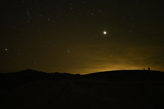 Starry sky with bright moon above landscape silhouette in Death Valley, California.