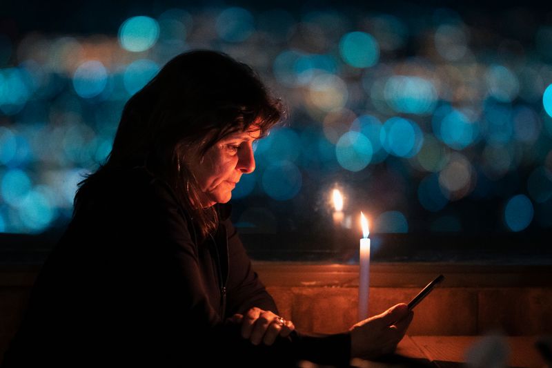 Senior woman using smartphone by candlelight in San José, Costa Rica, creates a cozy atmosphere.