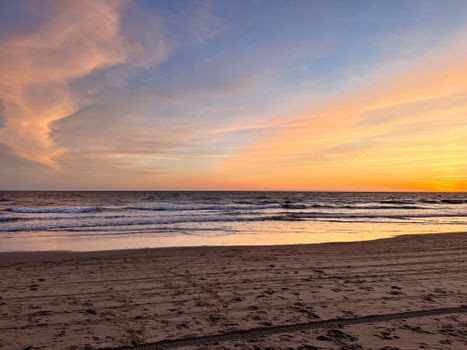 Serene beach at sunset with calm waves and a colorful sky reflecting on the sand.