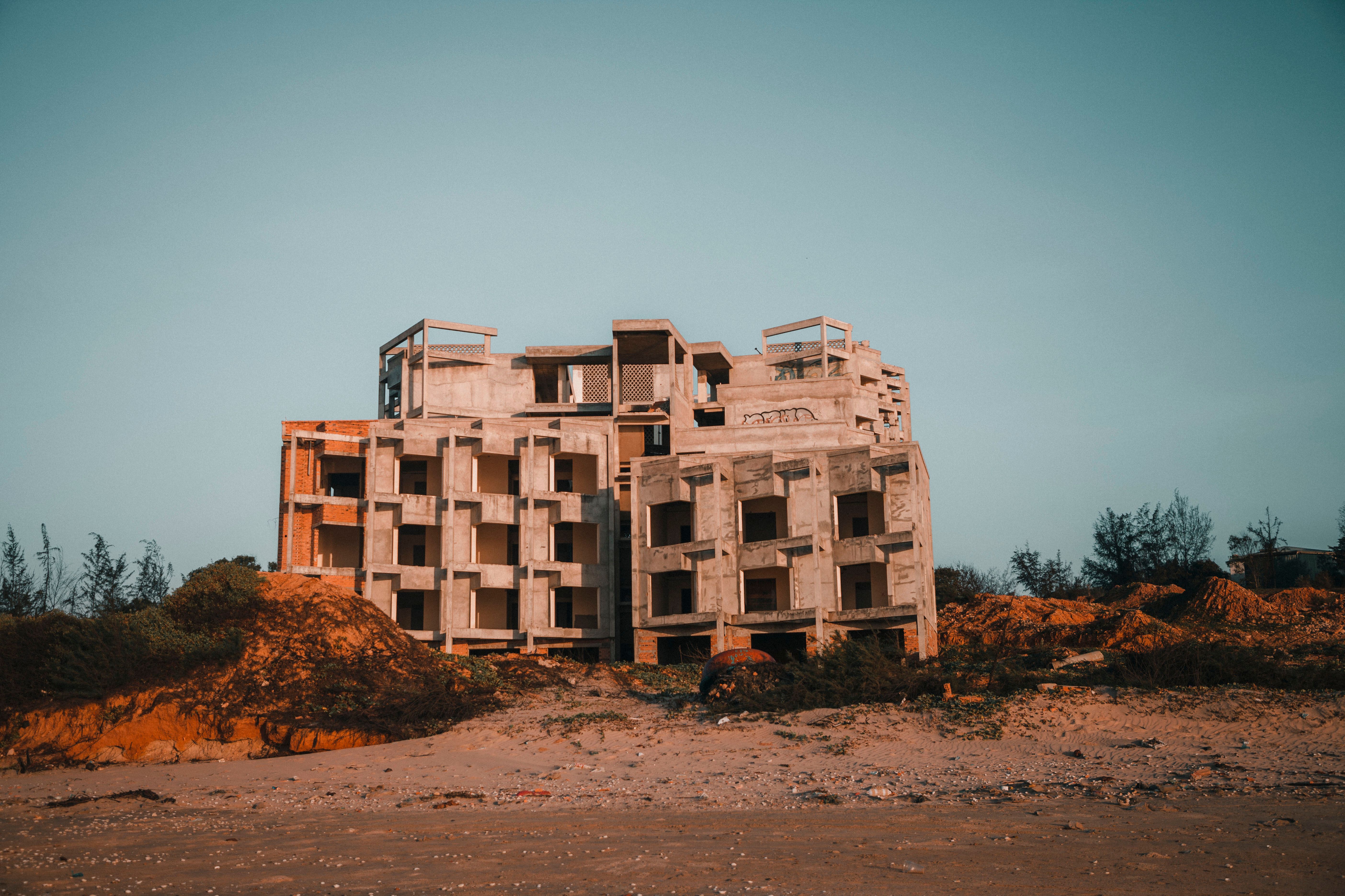 A concrete structure stands unfinished on a beach, surrounded by nature at sunset.