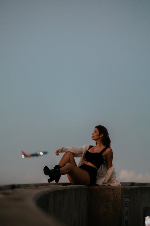 A woman sitting on a ledge with an airplane in the background