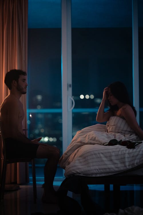 A man and woman are sitting on a bed in the dark