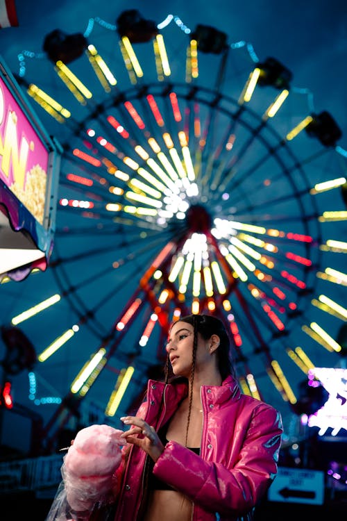 A woman in pink jacket and pink hat standing next to a ferris wheel