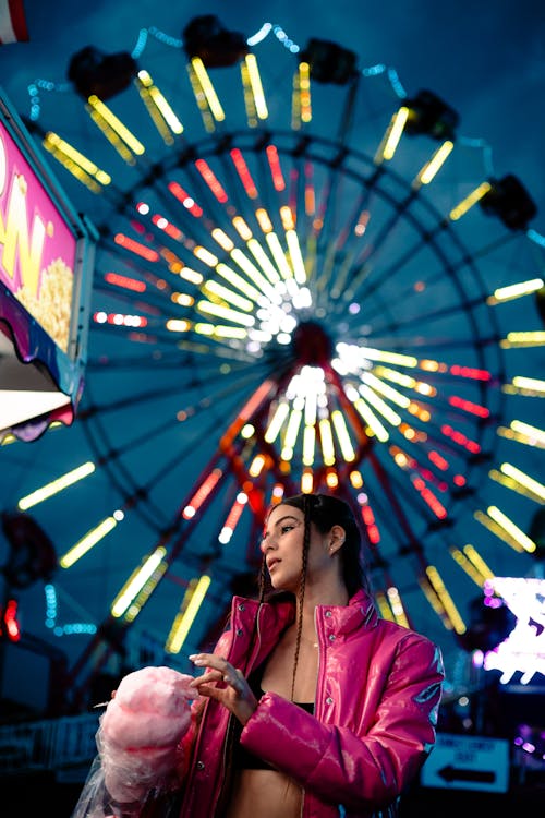 Free A woman in pink jacket and pink hat standing next to a ferris wheel Stock Photo