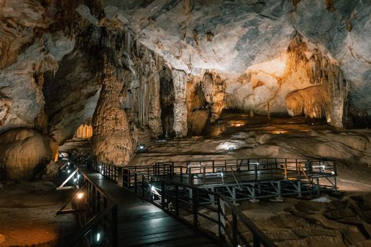 Explore the beauty of an illuminated cave with dramatic stalactites and a wooden walkway.