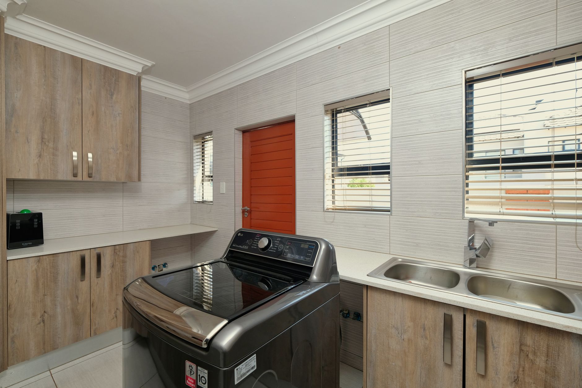 Spacious kitchen with wooden cabinets, washing machine, and dual sink. Bright and modern.