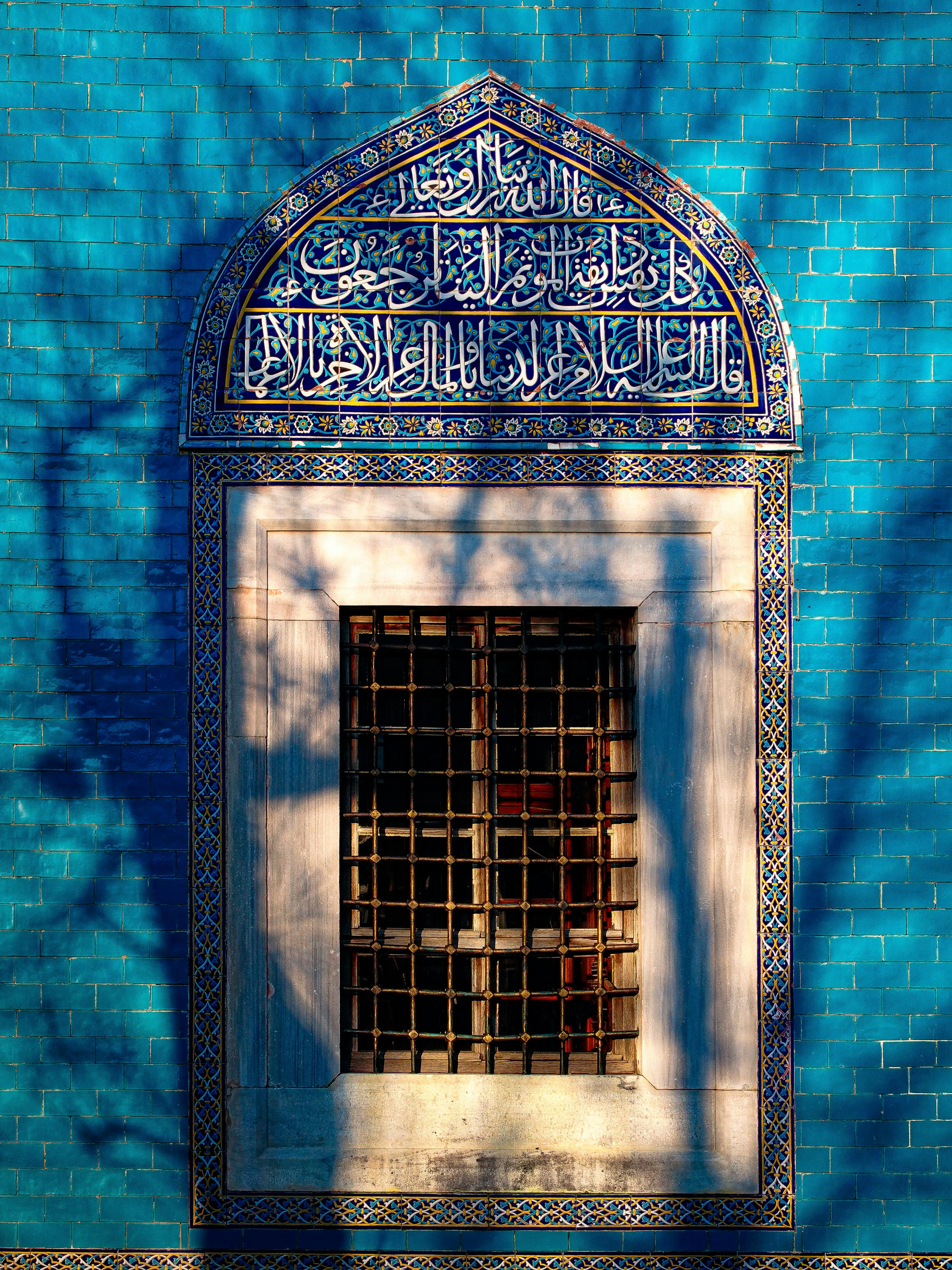 Blue tiled wall with intricate Arabic calligraphy and ornate window in Bursa, Türkiye.