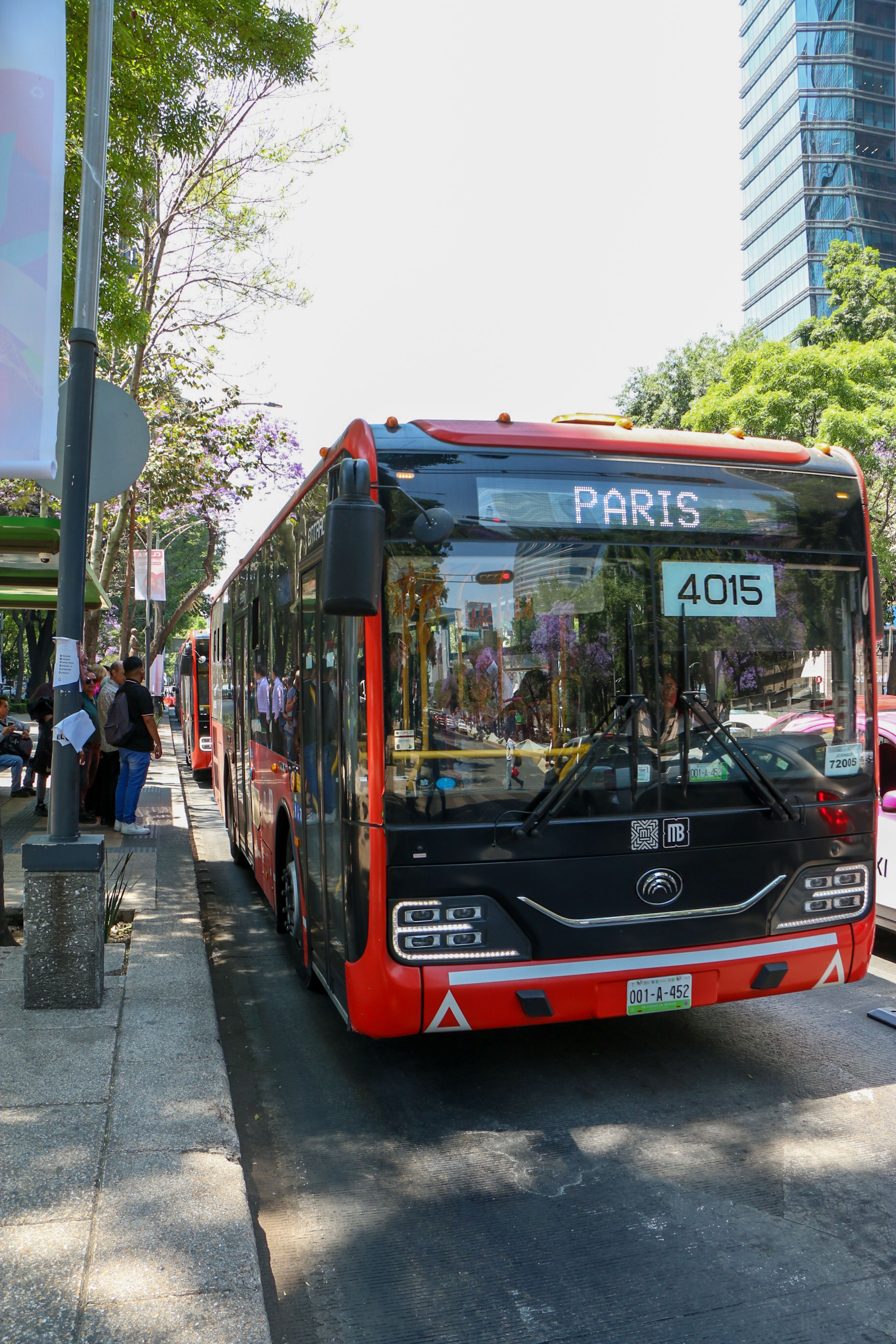 Red public bus named PARIS on urban street with city backdrop.