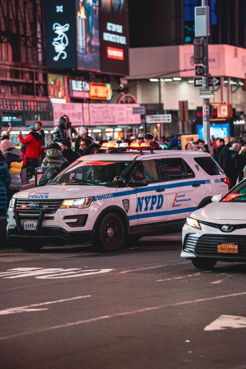 Free NYPD vehicle patrolling a busy city street in New York at night. Vibrant urban scene with city lights. Stock Photo
