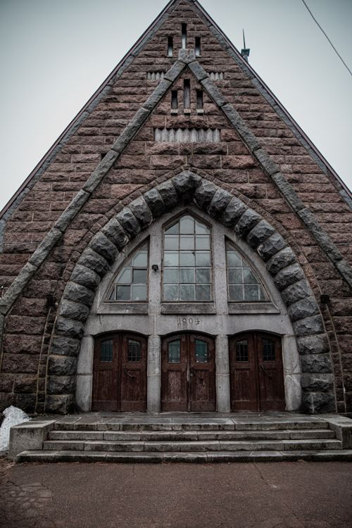 Free Front view of a historic stone church entrance with arched windows and wooden doors. Stock Photo