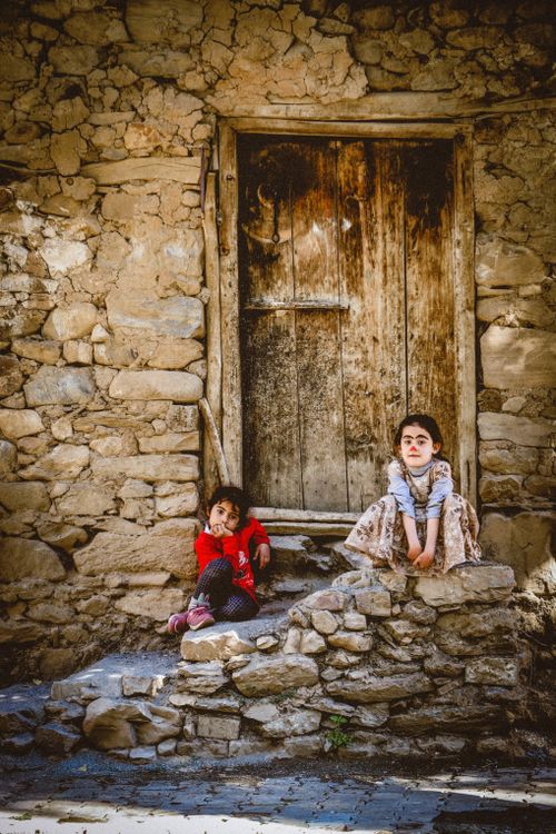 Free Two children sitting by a rustic wooden door, capturing the essence of rural Bahçesaray life. Stock Photo