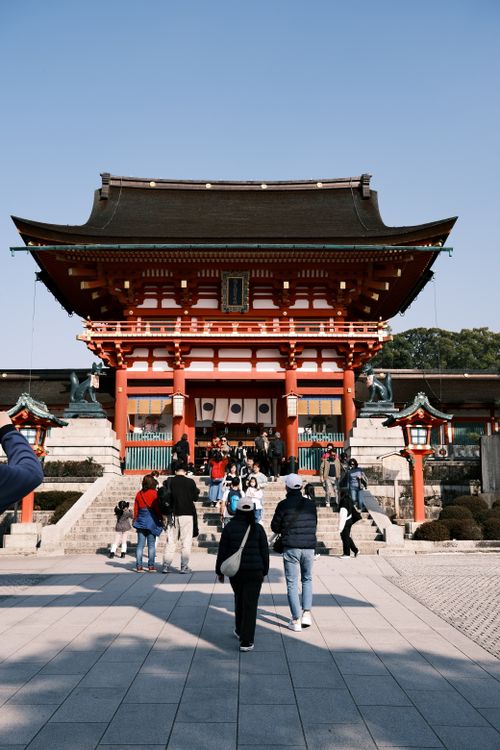 Free Visitors approaching the iconic Fushimi Inari-Taisha Shrine under a clear sky in Kyoto, Japan. Stock Photo