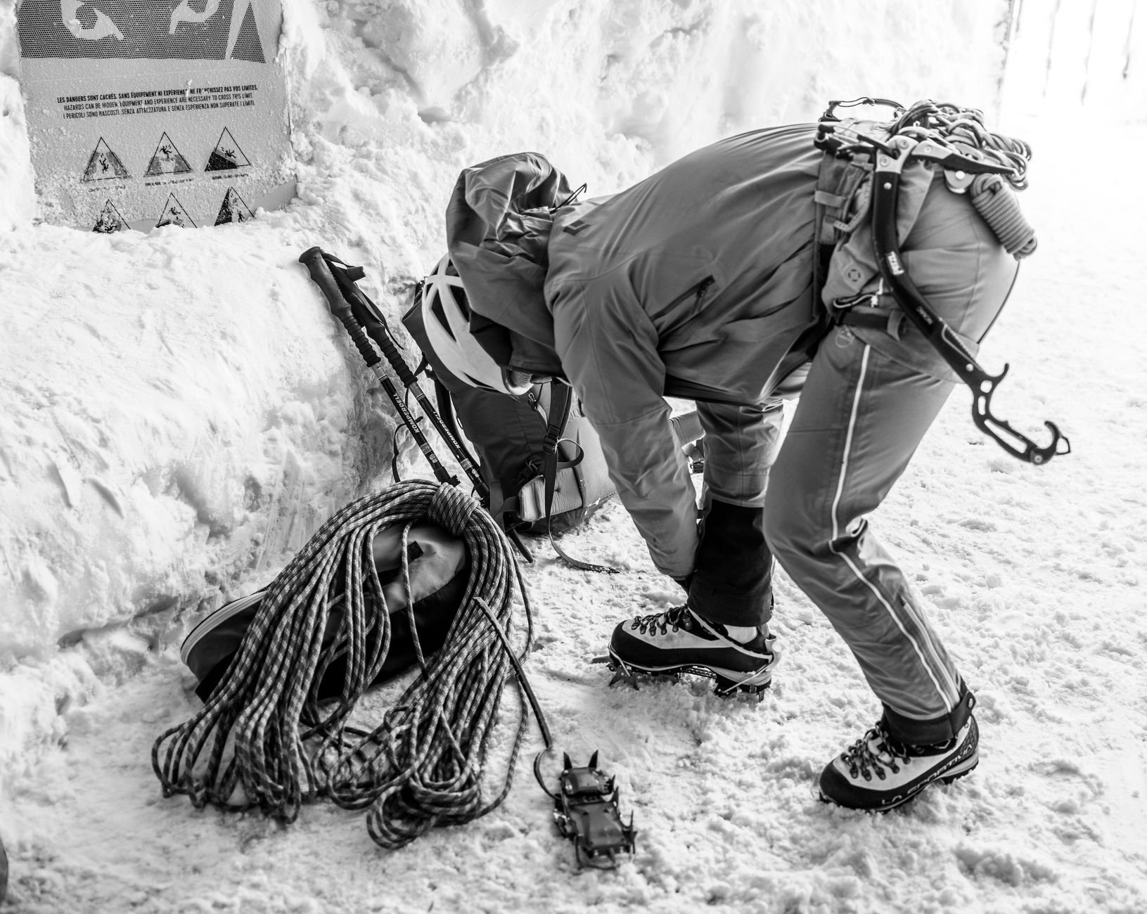 Mountaineer gears up on snow in Chamonix for a challenging winter climb. Black and white shot captures determination.