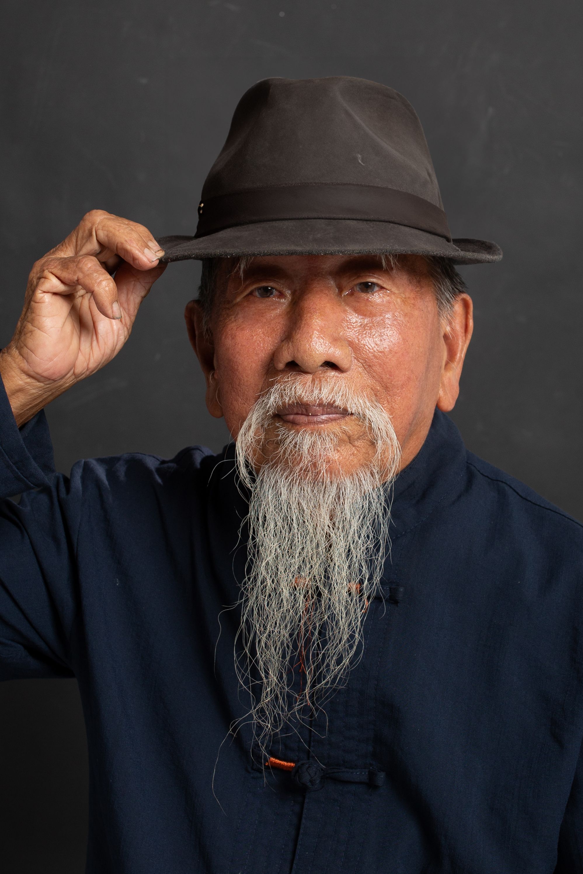 Portrait of an elderly man with a long beard, wearing a fedora and traditional attire.