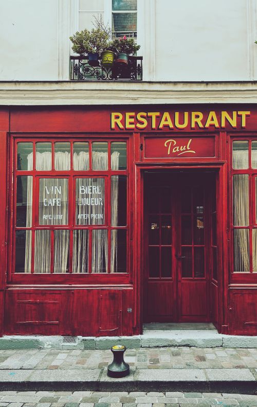 Free Vintage red facade of a Parisian restaurant with classic decor and signage. Captures Paris's charming street atmosphere. Stock Photo