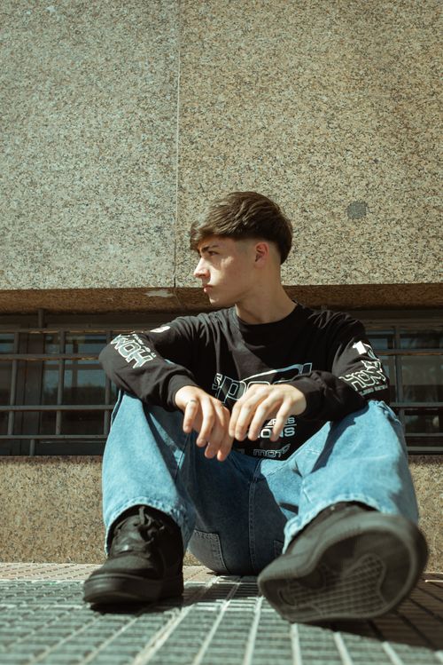 Free Teenager in casual fashion sitting on urban pavement, showcasing style in city setting. Stock Photo
