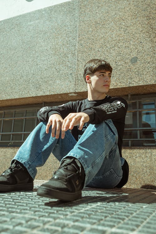 A young man sitting on the ground in front of a building