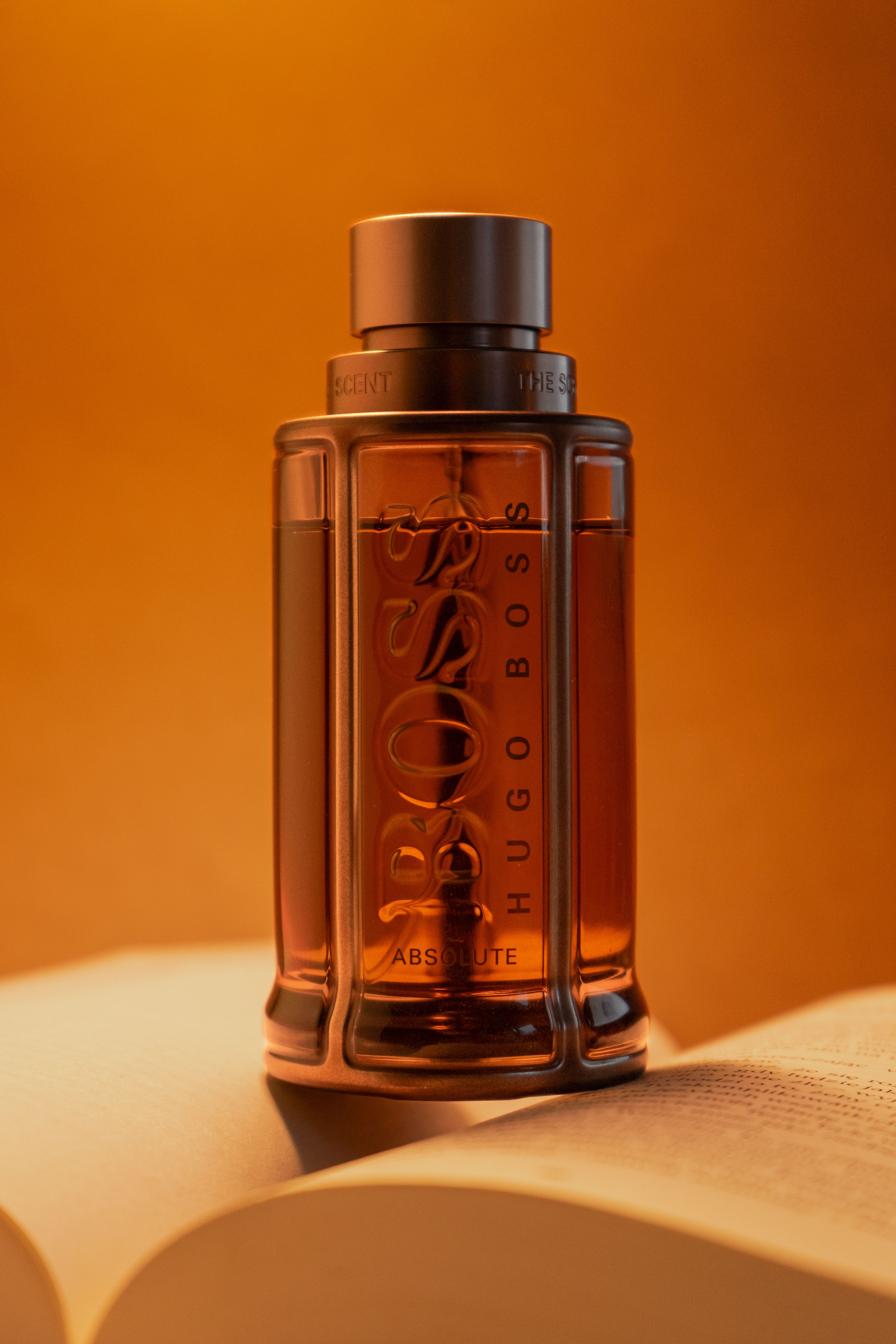 A luxury perfume bottle displayed elegantly on an open book with an orange backdrop.