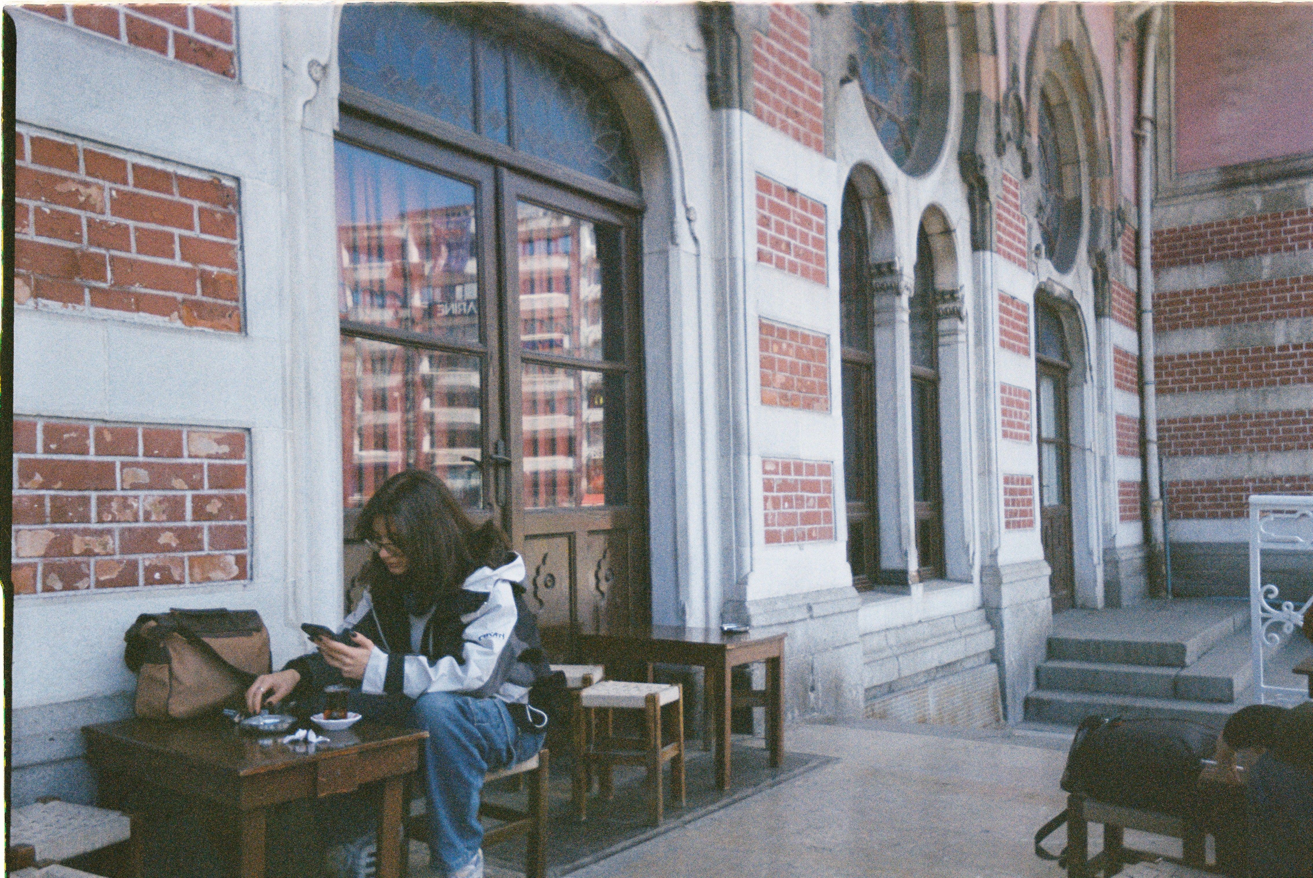 A woman enjoys a quiet moment at a cafe with historical architecture in the background.