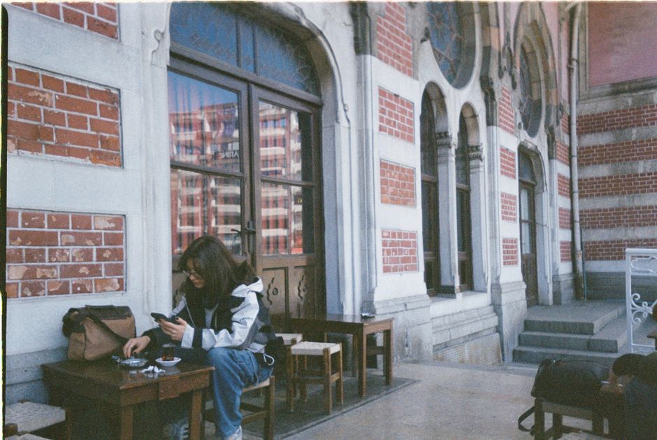 A woman enjoys a quiet moment at a cafe with historical architecture in the background.
