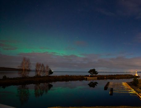 Breathtaking view of the aurora borealis reflecting on a serene lake under a starry night sky.