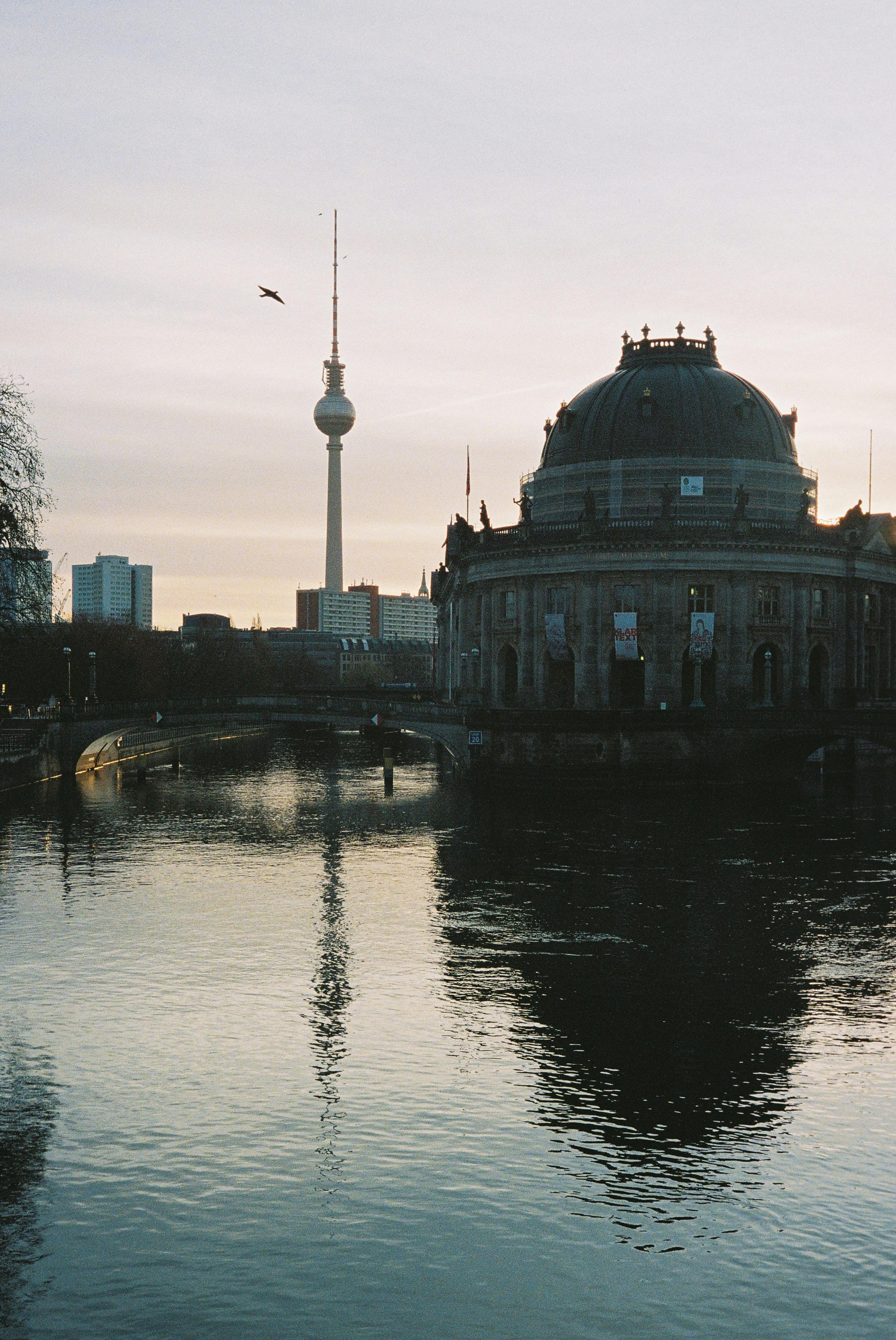 A serene view of Bode Museum and Berlin TV Tower reflected in the Spree River at sunset.