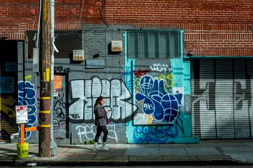 Free A woman walks past a colorful mural and graffiti on a city street wall. Stock Photo