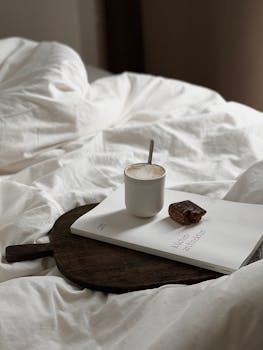 Serene morning scene with a coffee cup, book, and snack on a cozy bed setting.