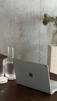 Minimalist setup of a laptop with glasses and a decanter on a wooden table against a gray background.