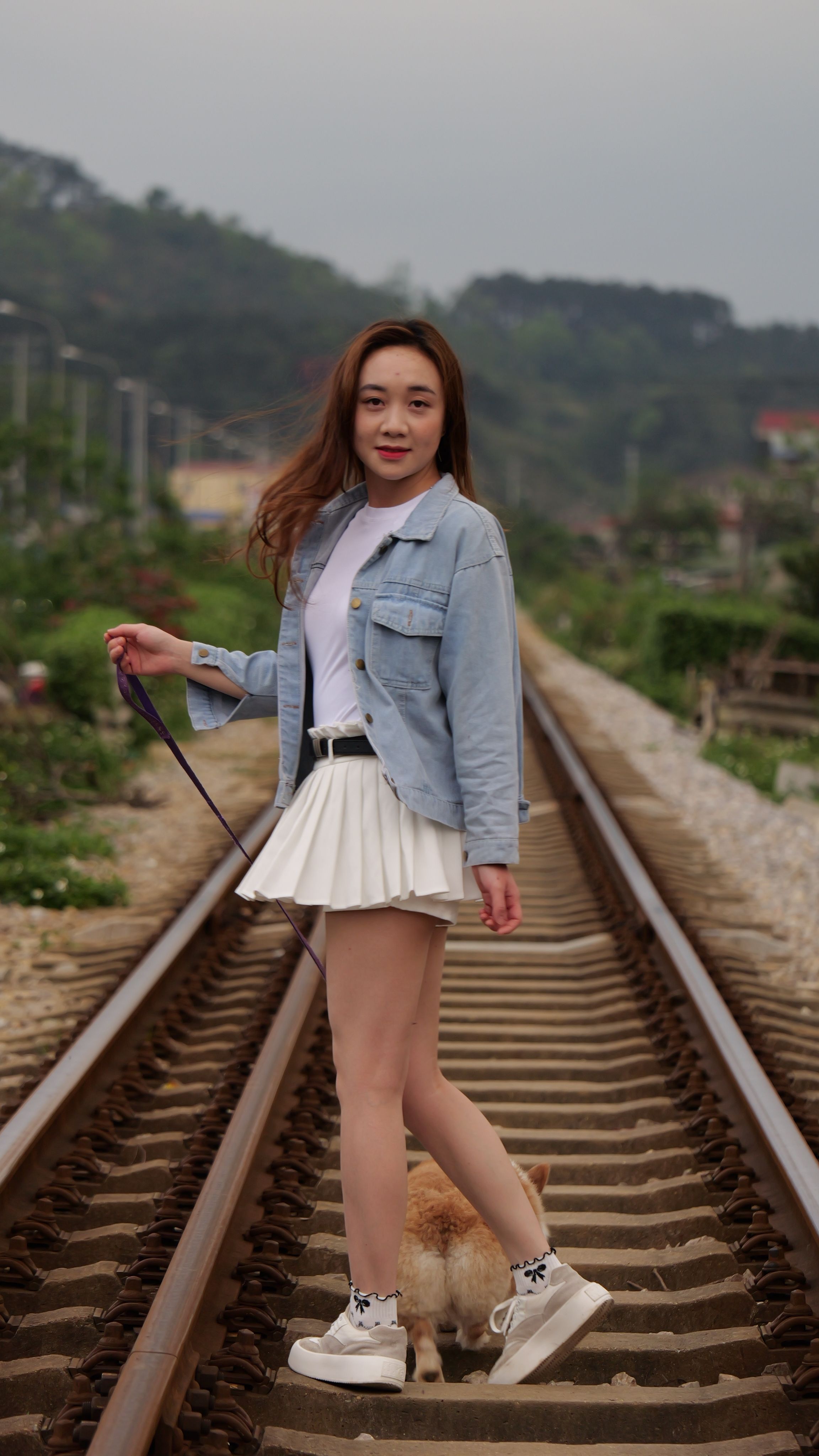 A young woman with a corgi on a railway track during summer. Outdoors and playful vibe.