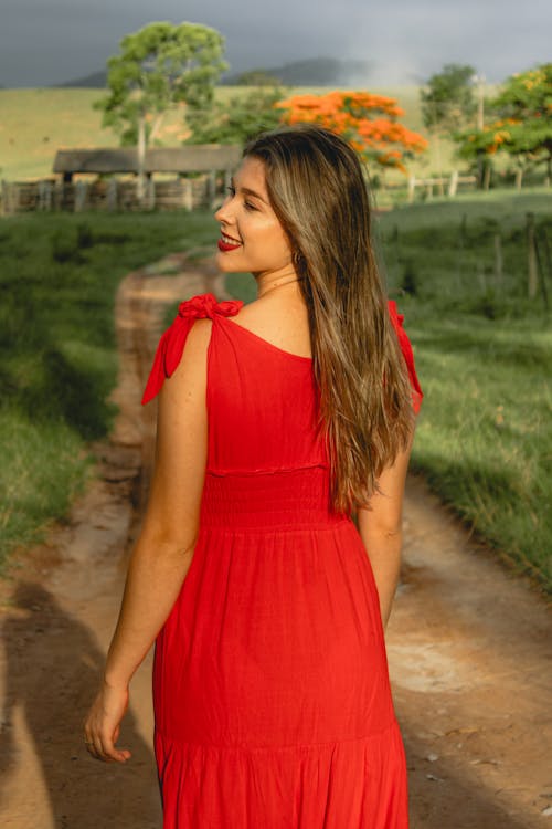 A woman in a red dress walking down a dirt road