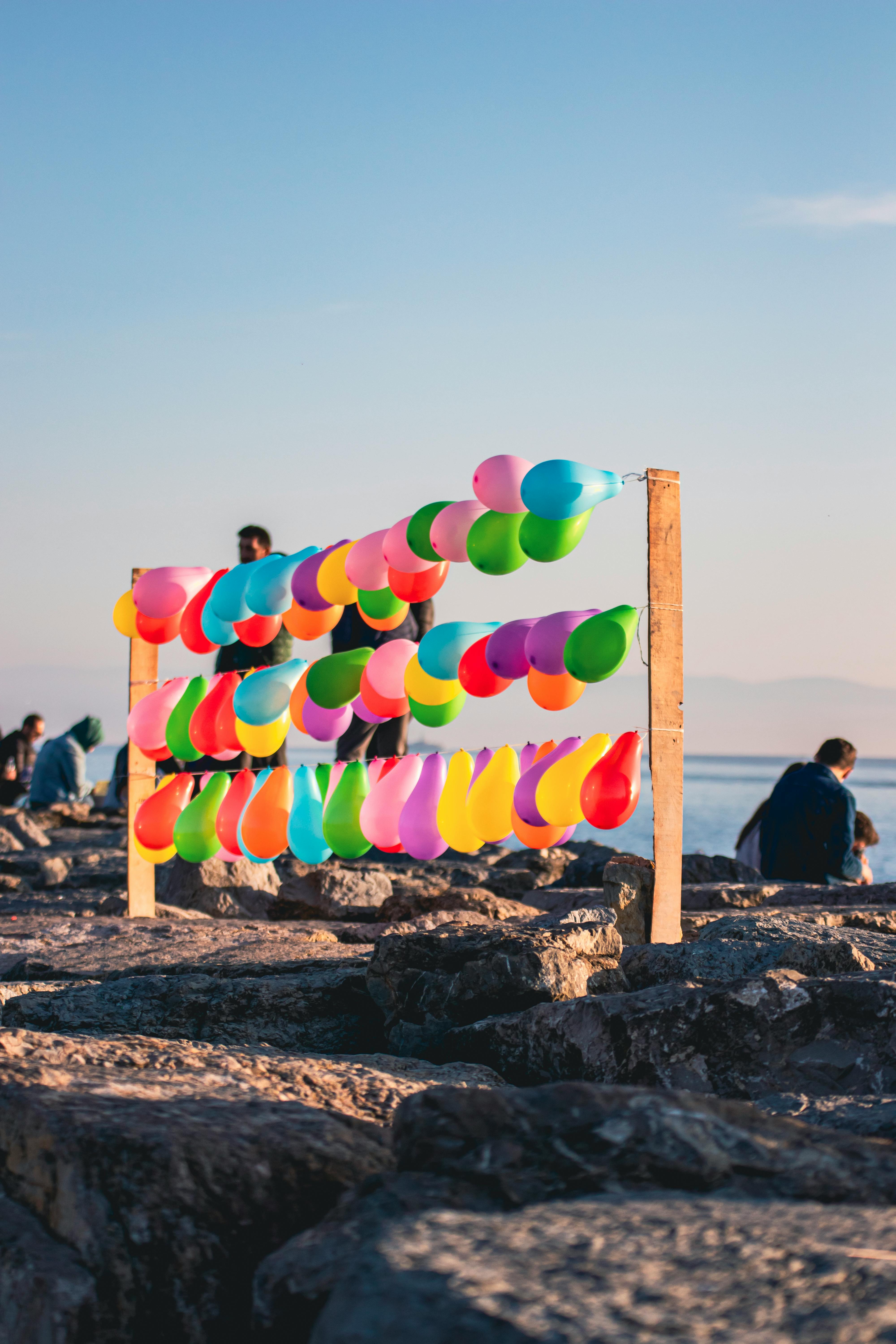 A vibrant display of colorful balloons on the rocky coast with a serene sea backdrop at sunset.