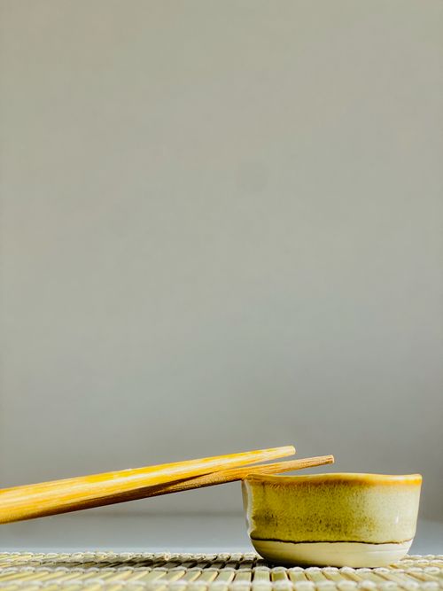 Free A simple ceramic bowl with chopsticks on a woven mat against a gray background, showcasing Asian dining culture. Stock Photo