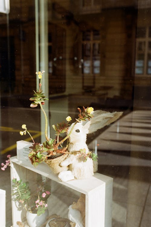 A small white rabbit sits on a shelf in front of a window