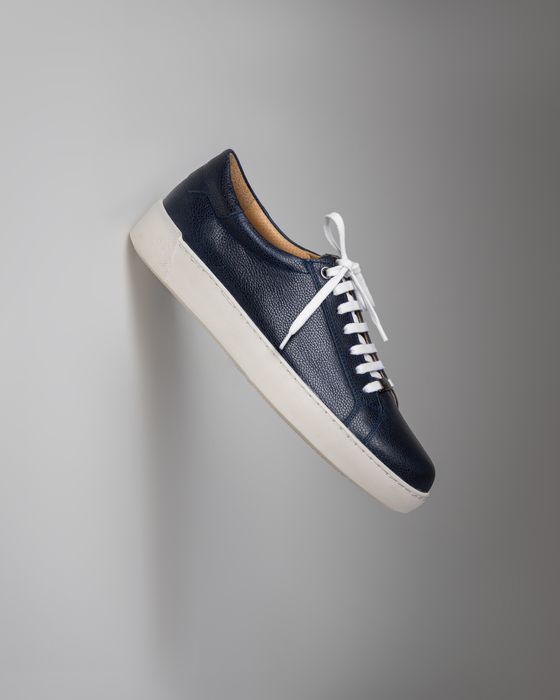 Navy leather low-top sneaker against a pale wall, photo by saeed karimi on Pexels