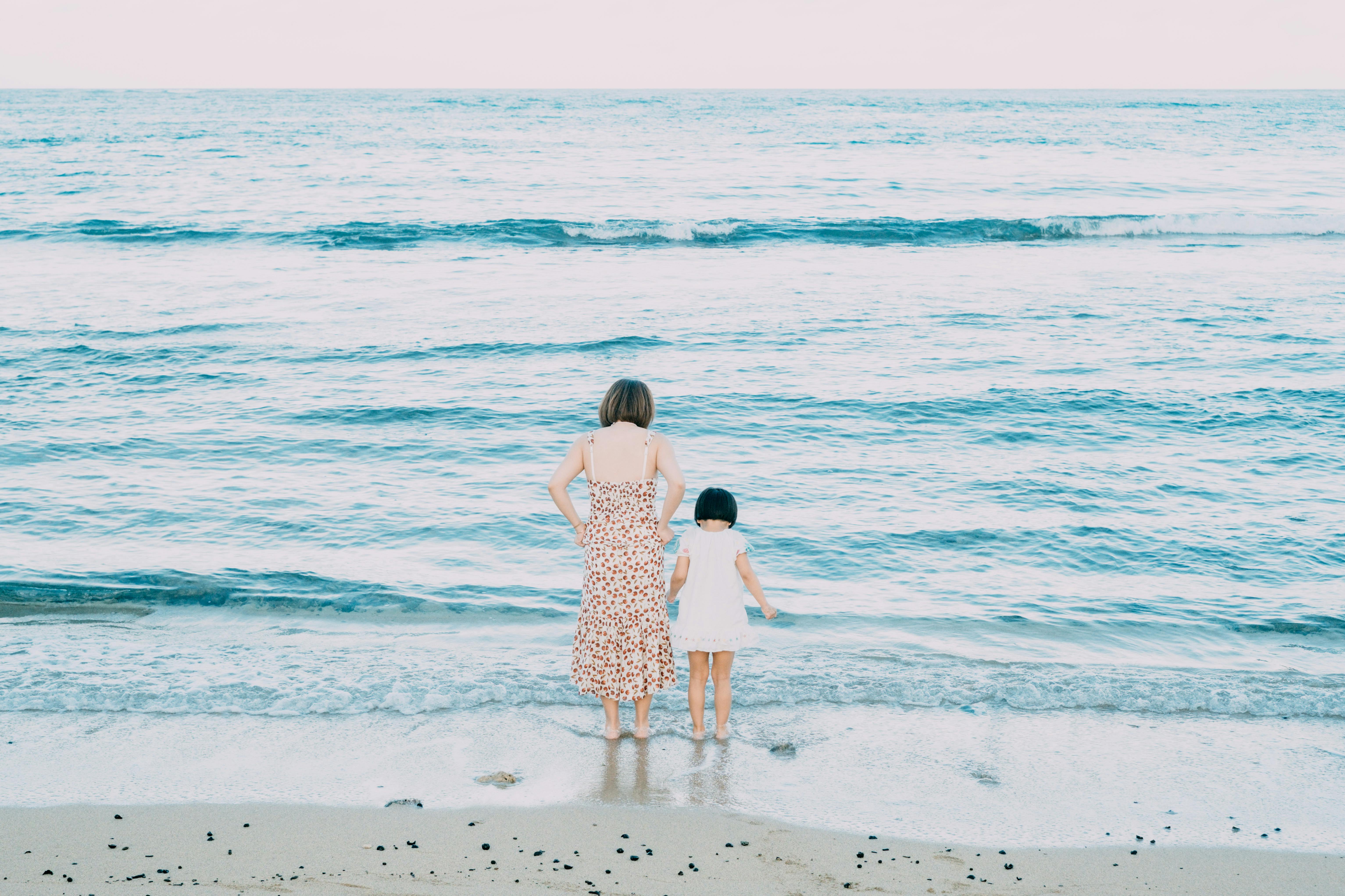 A serene moment of a mother and daughter standing at the beach, enjoying the ocean view.