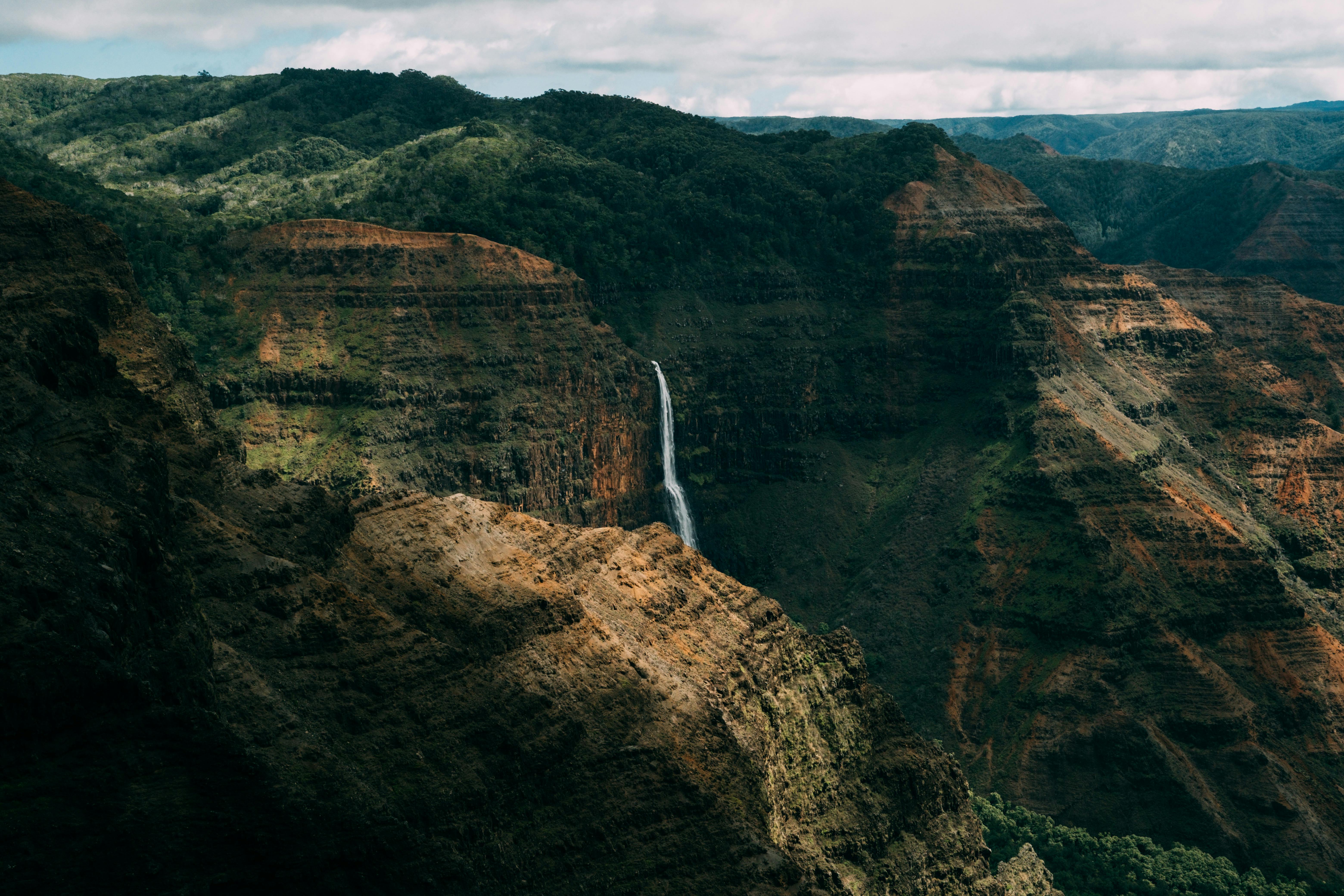 Breathtaking view of Waimea Canyon with a stunning waterfall in the foreground, showcasing the natural beauty of Hawaii.