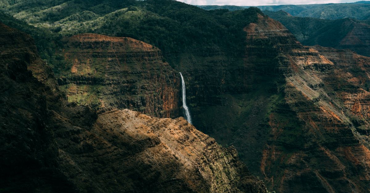 Photo by Michael Li Breathtaking view of Waimea Canyon with a stunning waterfall in the foreground, showcasing the natural beauty of Hawaii.